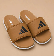 A pair of Adidas slide sandals in tan with black logo details and white soles, displayed on a solid tan background.