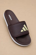 A single Adidas slide sandal in dark brown with a textured strap, featuring the brand's logo in light green on the strap and the 'adidas' wordmark on the footbed, set against a solid beige background.