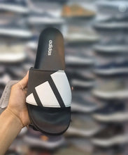 A hand holds an Adidas slide sandal with a black and white design