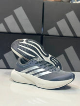 A pair of Charcoal Silver Adidas Supernova Rise 3 in dark gray and white, with one shoe standing upright and the other lying on its side to show the sole. The Adidas logo is clearly visible on the side of the shoe, and the shoes are positioned in front of their branded shoeboxes.