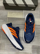 Blue Orange Adidas Supernova Rise 3  on a tiled floor with an Adidas box in the background.