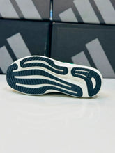 A close-up of a White Green Adidas Supernova Rise 3  outsole showing a white and dark navy textured tread pattern, set against a background of dark shoeboxes with a white surface.
