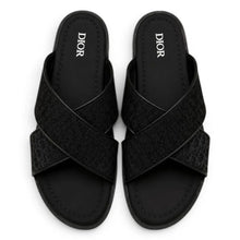 A pair of black Christian Dior slide sandals with textured, embossed crossover straps, shown from a top-down view on a white background.