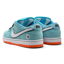 A pair of Nike Dunk Low sneakers in light blue suede with a white Swoosh, a white midsole, and a bright orange outsole, shown against a plain white background.