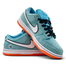 A pair of Nike Dunk Low sneakers in light blue suede with white and light pink Swooshes, black laces, and bright orange outsoles, shown on a white background.
