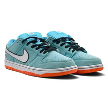 A pair of Nike Dunk Low sneakers in light blue suede with black laces, a white Swoosh, and an orange outsole, shown on a white background.