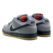 A pair of Nike low-top sneakers in gray suede and leather, featuring a dark green Swoosh, black heel tab, and a gum sole.